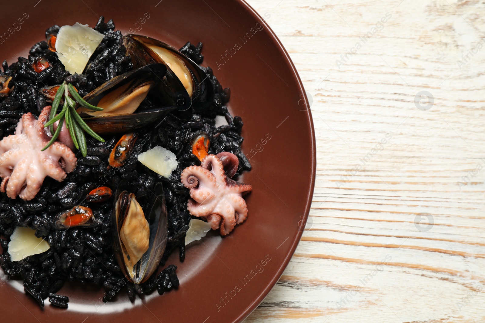 Photo of Delicious black risotto with seafood on white wooden table, top view