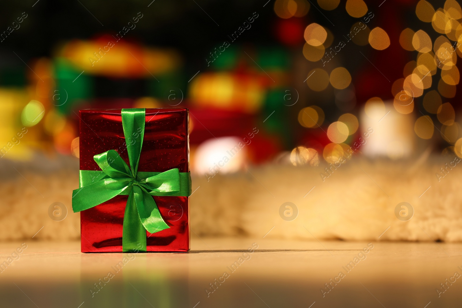 Photo of Beautiful Christmas gift with green bow on floor in room, space for text