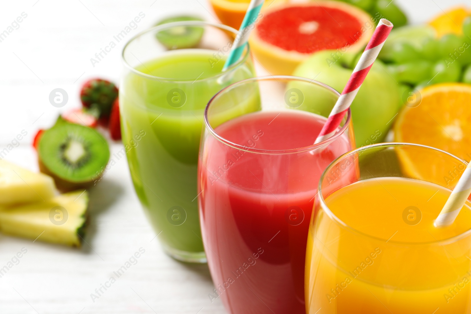 Photo of Glasses of different juices with straws and fresh fruits on wooden table, closeup. Space for text