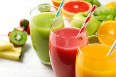 Glasses of different juices with straws and fresh fruits on wooden table, closeup. Space for text