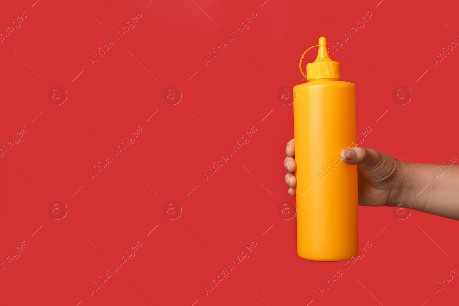 Photo of Woman with bottle of mustard on red background, closeup