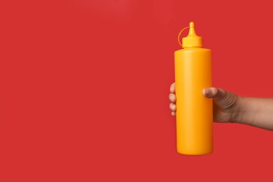 Photo of Woman with bottle of mustard on red background, closeup