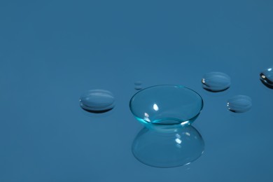 Photo of Contact lens and drops of water on blue reflective surface. Space for text