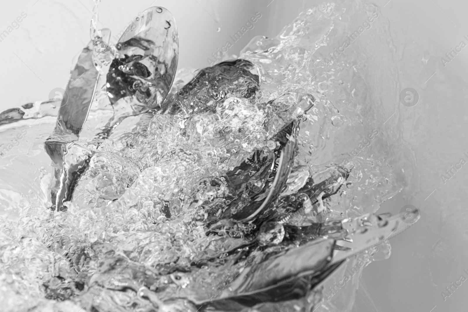 Photo of Washing silver spoons, forks and knives under stream of water in kitchen sink, above view