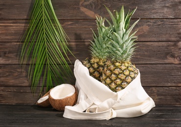 Photo of Fresh pineapples and coconut on table against wooden wall