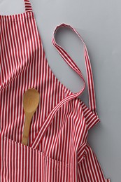 Photo of Red striped apron with wooden spoon on light grey background, top view