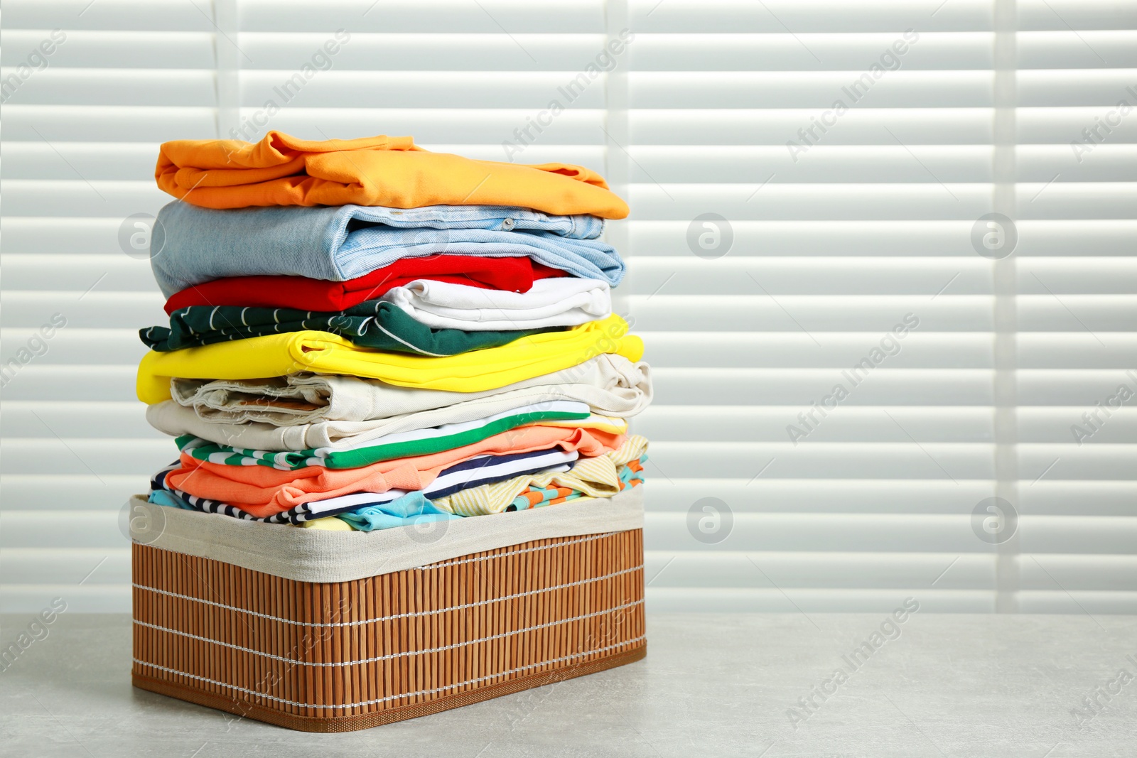 Photo of Laundry basket with clean clothes on light grey table indoors. Space for text