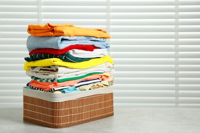 Photo of Laundry basket with clean clothes on light grey table indoors. Space for text