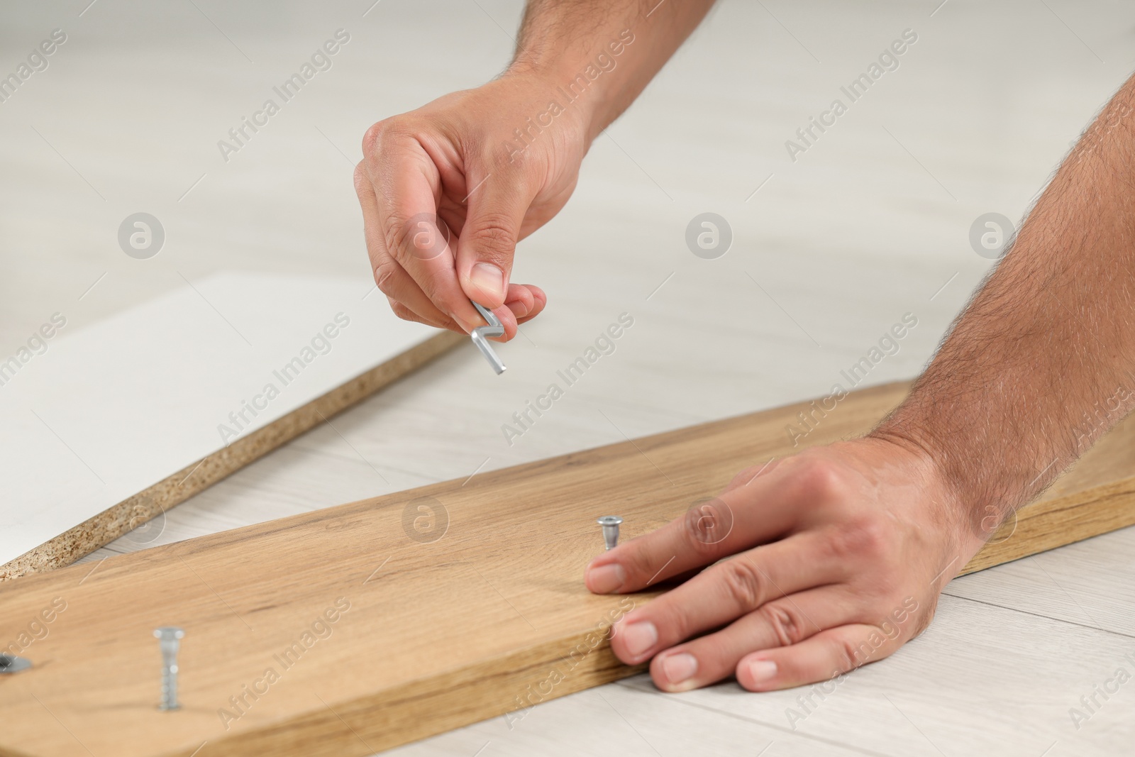 Photo of Man with hex key assembling furniture on floor indoors, closeup