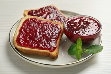 Photo of Delicious toasts served with jam and mint on white wooden table, closeup