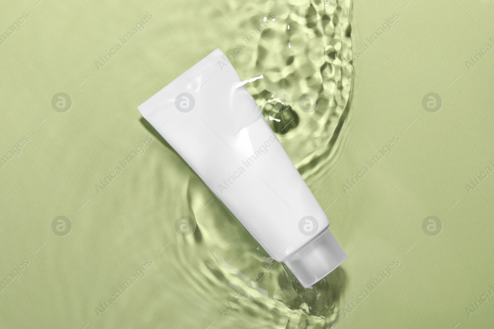 Photo of Tube of facial cleanser in water against olive background, top view