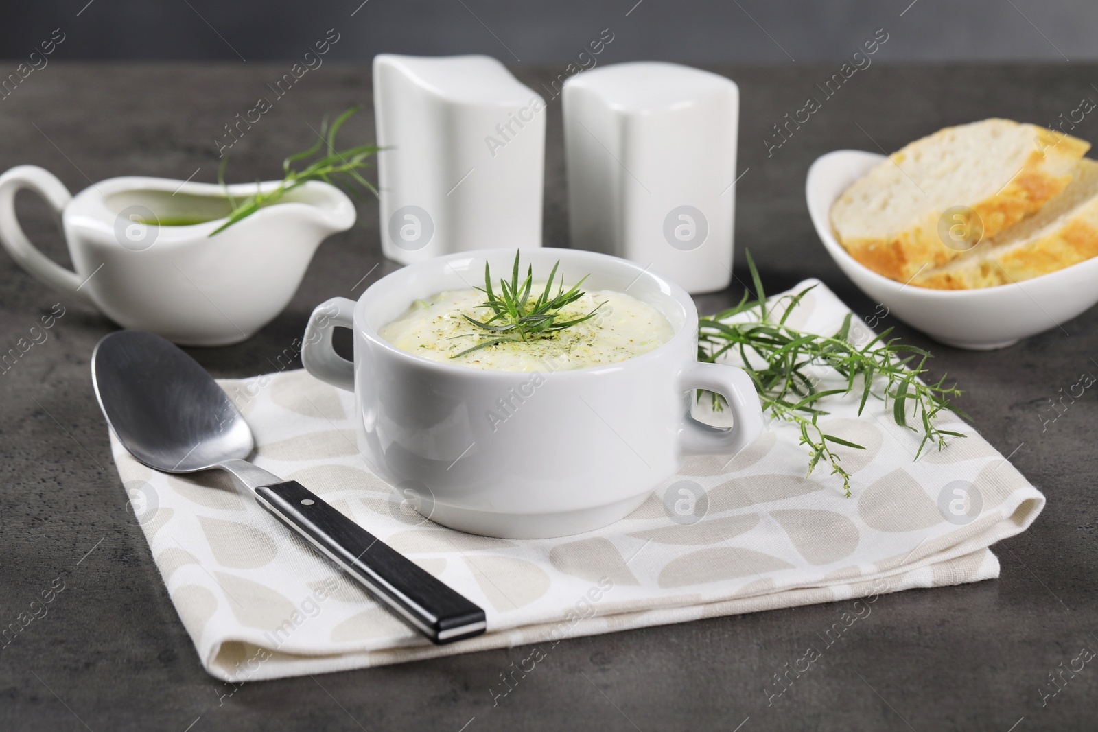 Photo of Delicious cream soup with tarragon, spices and potato in bowl served on dark textured table