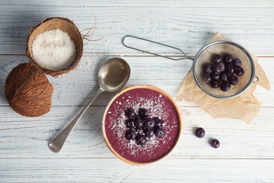 Flat lay composition with bowl of tasty acai smoothie on wooden table