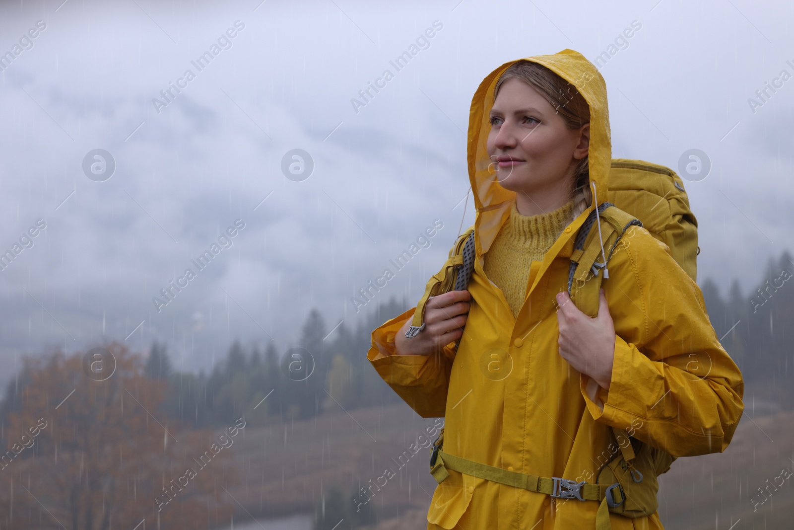 Photo of Young woman in raincoat enjoying mountain landscape under rain