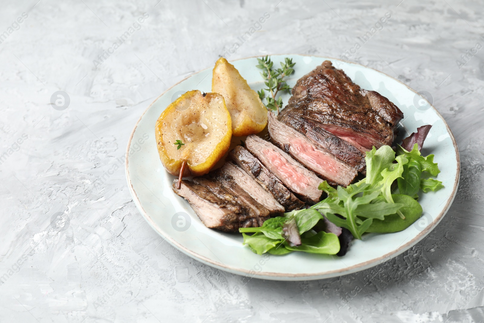 Photo of Pieces of delicious roasted beef meat, caramelized pear and greens on light textured table