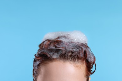 Young woman with shampoo foam on her head against light blue background, closeup. Space for text