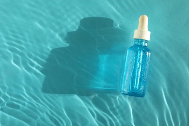 Bottle of cosmetic serum in water on turquoise background, top view. Space for text