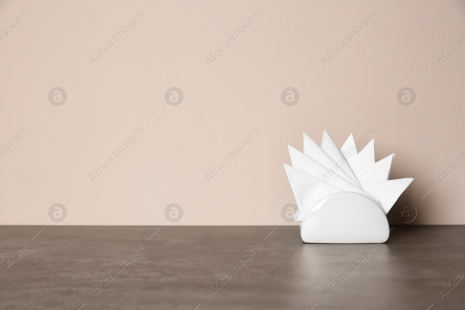 Photo of Napkin holder with paper serviettes on table against color background. Space for text