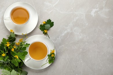 Photo of Cups of aromatic celandine tea and flowers on grey table, flat lay. Space for text