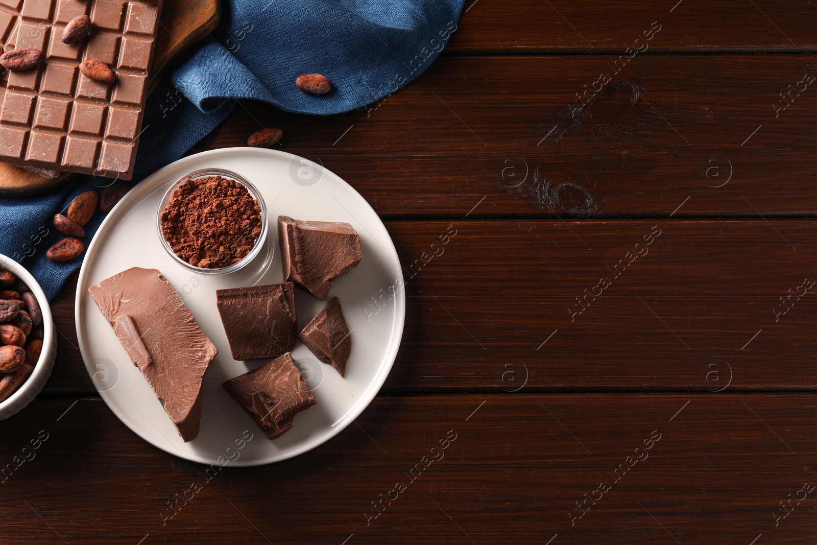 Photo of Pieces of tasty milk chocolate, cocoa beans and powder on wooden table, flat lay. Space for text