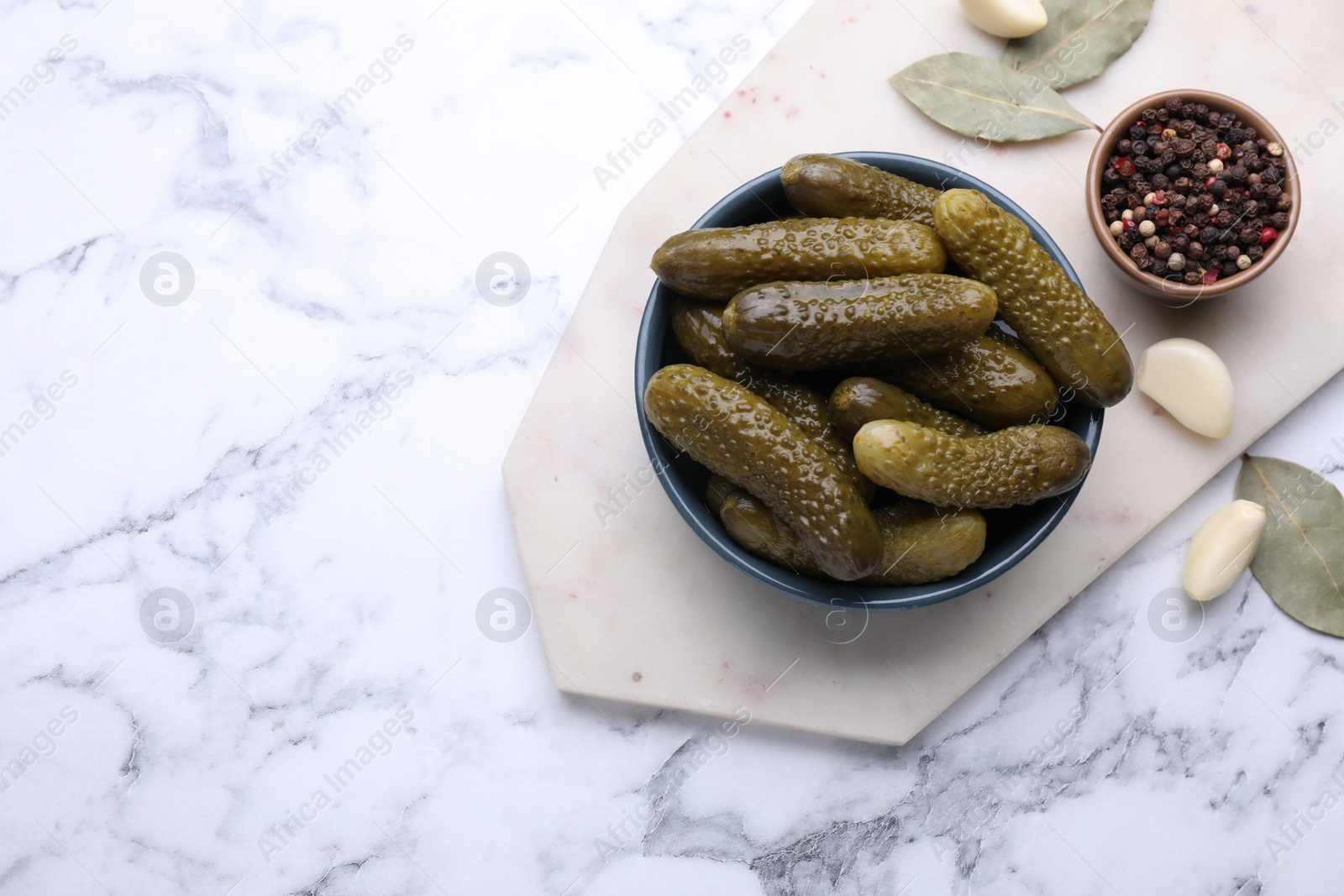 Photo of Bowl of pickled cucumbers and ingredients on white marble table, flat lay. Space for text