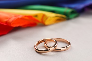 Photo of Rainbow LGBT flag and wedding rings on white background, closeup