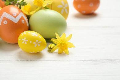 Photo of Colorful Easter eggs and flowers on white wooden table
