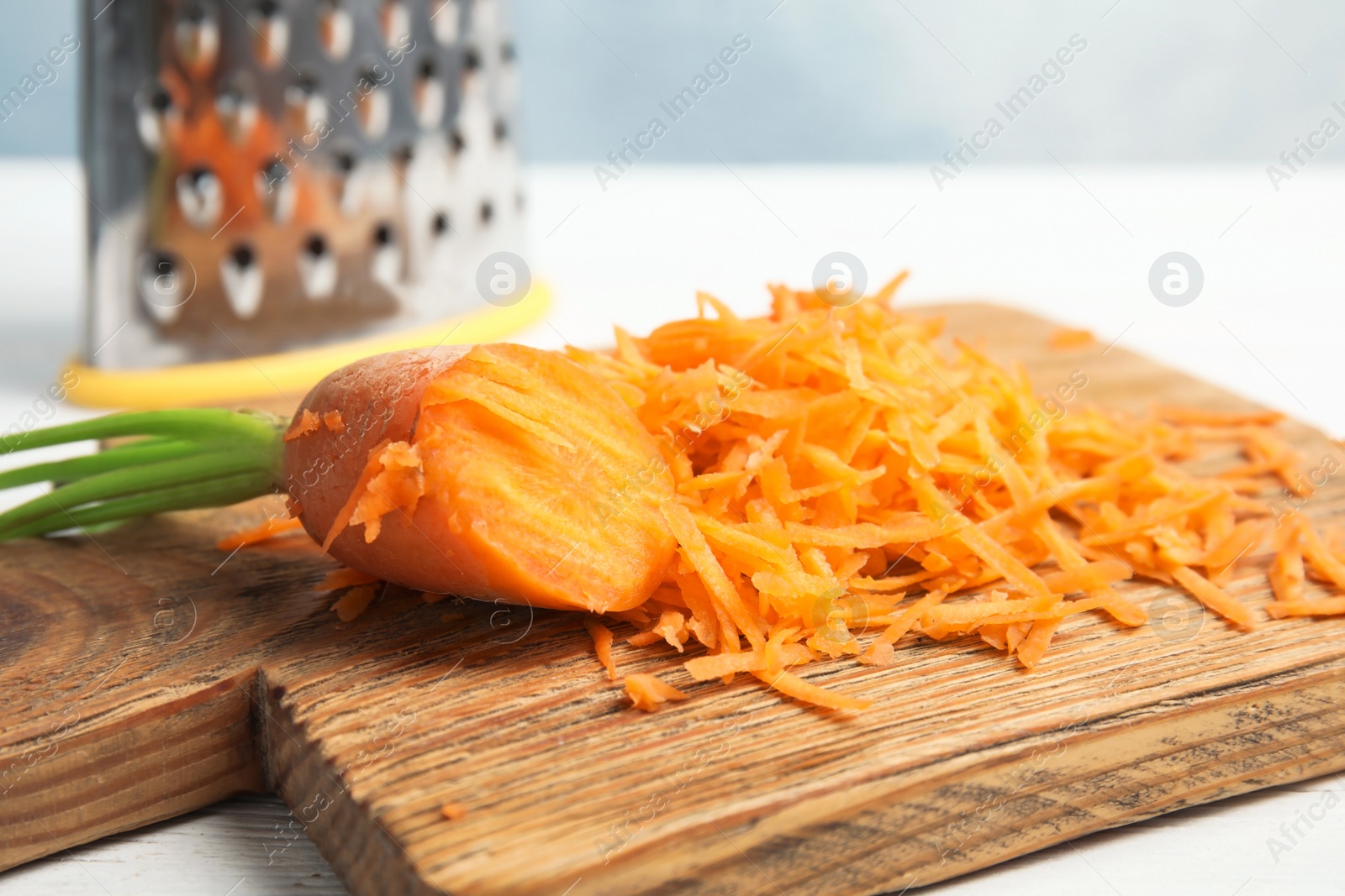 Photo of Wooden board with grated carrot on table, closeup