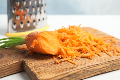 Wooden board with grated carrot on table, closeup