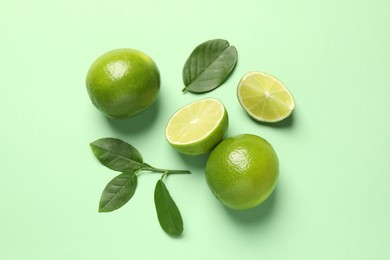 Whole and cut fresh ripe limes with leaves on light green background, flat lay