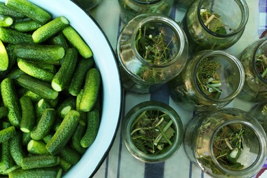 Photo of Glass jars with different herbs and fresh cucumbers on table, flat lay. Pickling vegetables