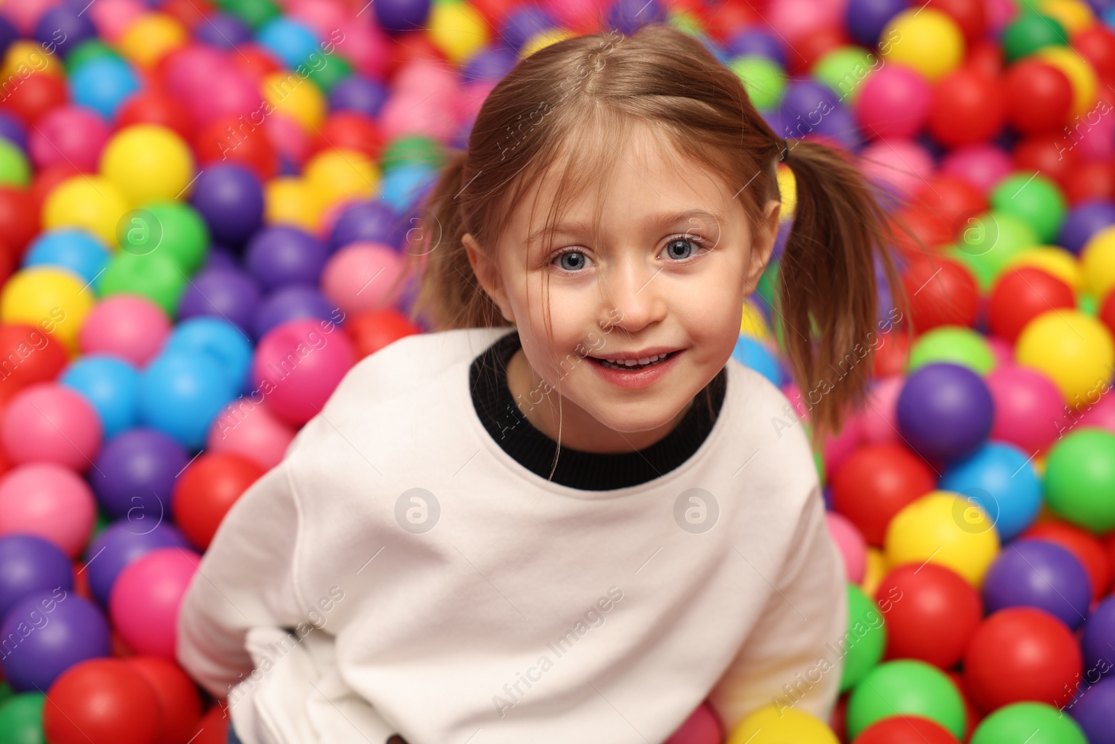 Photo of Happy little girl sitting on colorful balls in ball pit