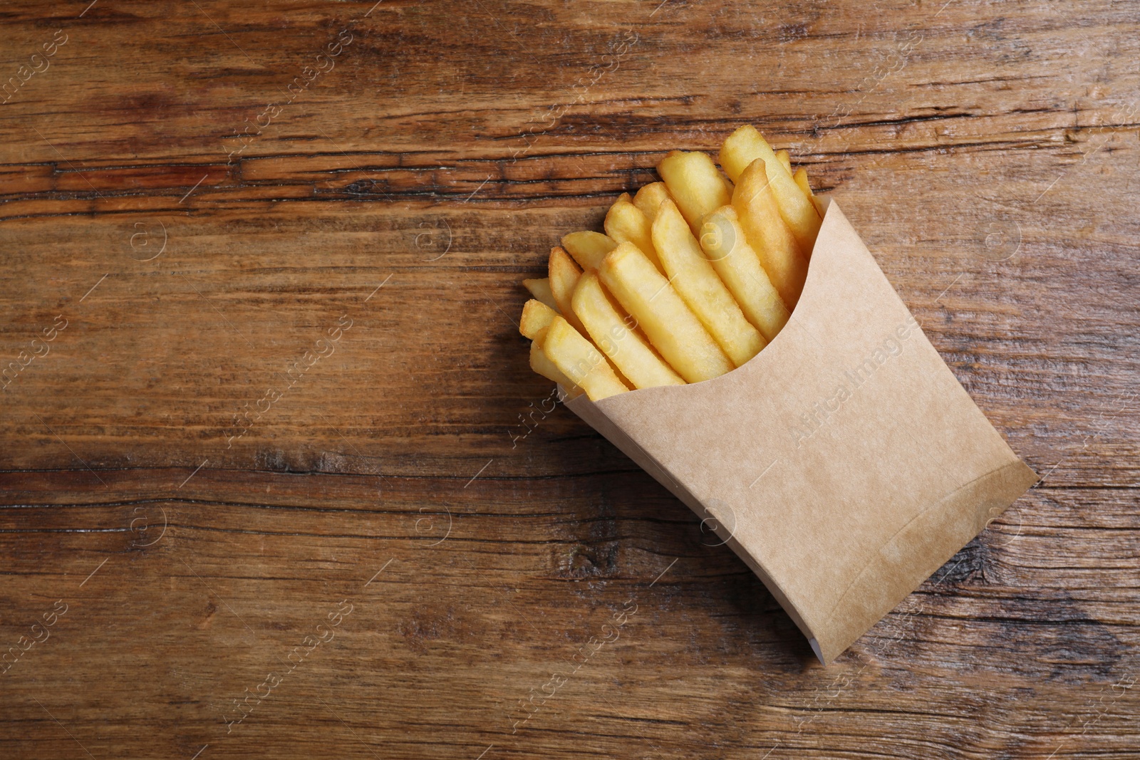 Photo of Delicious french fries in paper box on wooden table, top view. Space for text