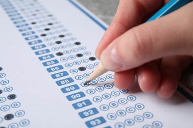 Student filling answer sheet at table, closeup. Passing exam