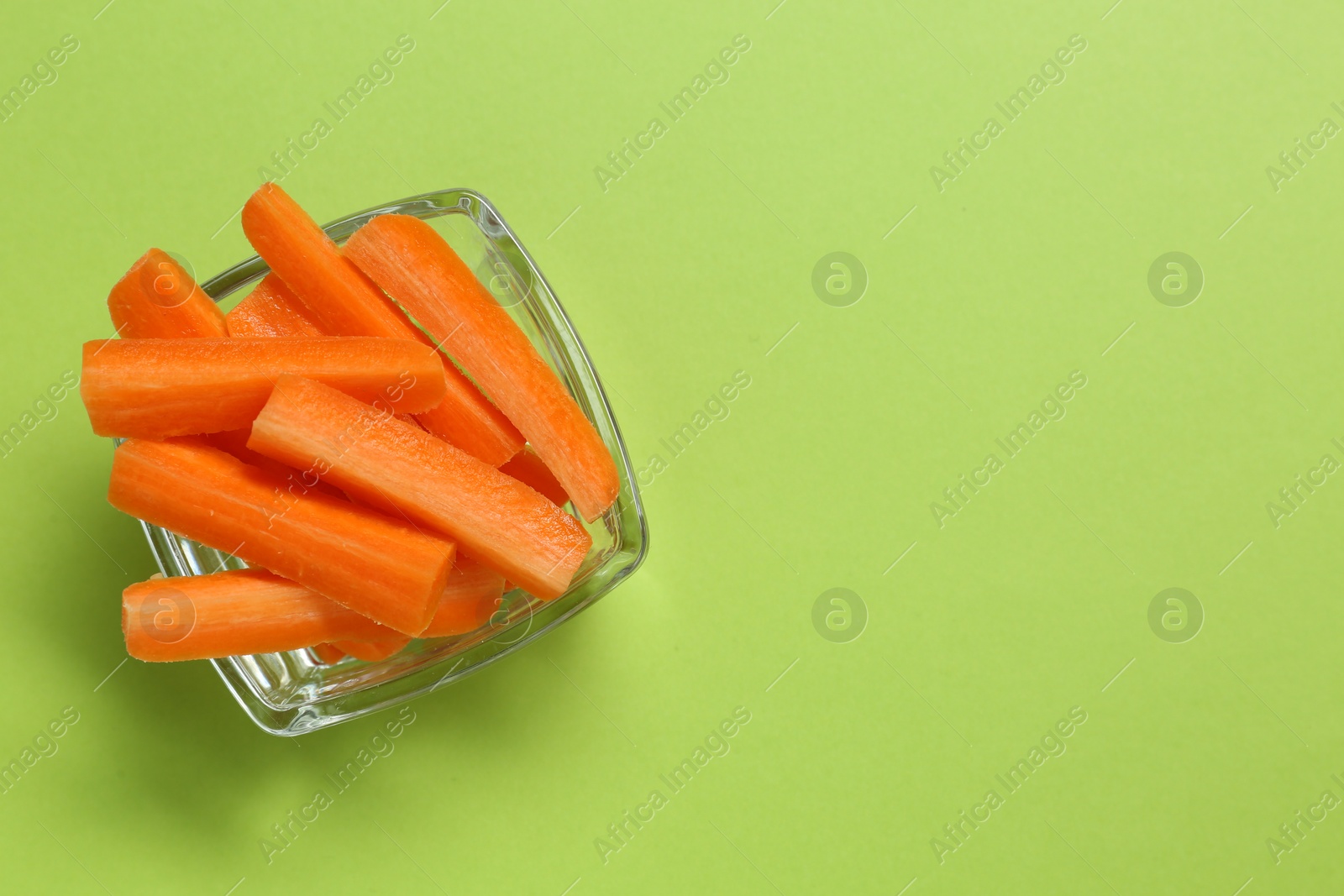 Photo of Cut fresh carrot in bowl and space for text on green background, top view. Finger food