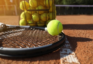 Photo of Tennis ball, racket and basket on clay court, closeup