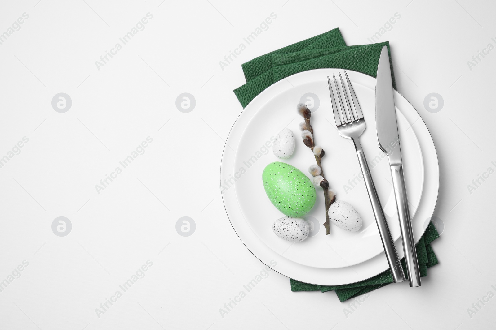 Photo of Festive table setting with willow twig and painted eggs on white background, top view with space for text. Easter celebration