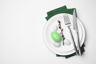 Photo of Festive table setting with willow twig and painted eggs on white background, top view with space for text. Easter celebration