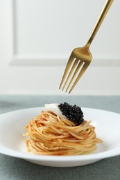 Photo of Eating tasty spaghetti with tomato sauce and black caviar at table, closeup. Exquisite presentation of pasta dish