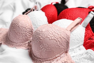 Photo of Beautiful lace bras on white bed sheet, closeup. Stylish underwear