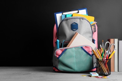 Photo of Backpack with different school stationery on grey wooden table near blackboard, space for text