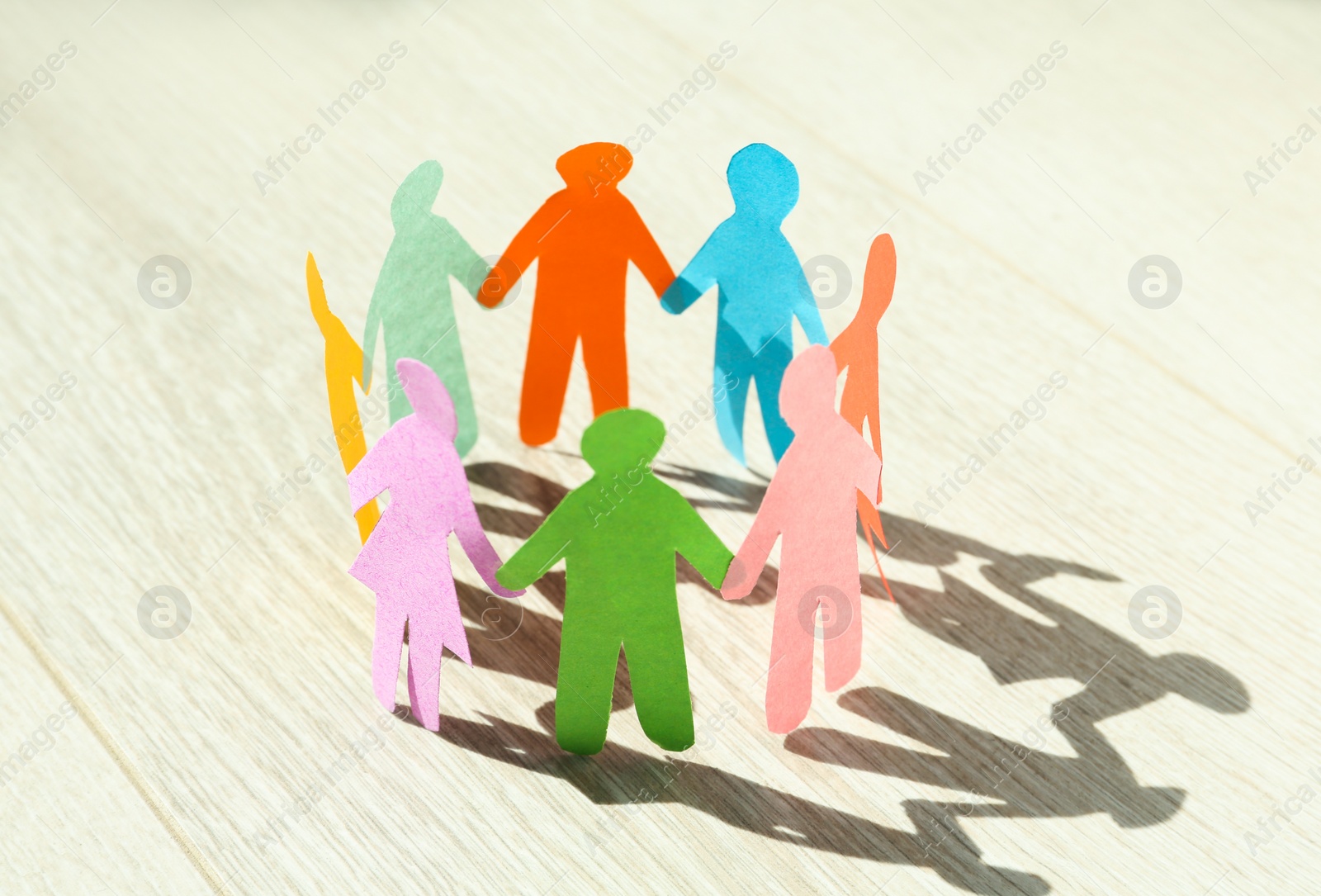 Photo of Many different paper human figures standing in circle on white wooden table. Diversity and inclusion concept