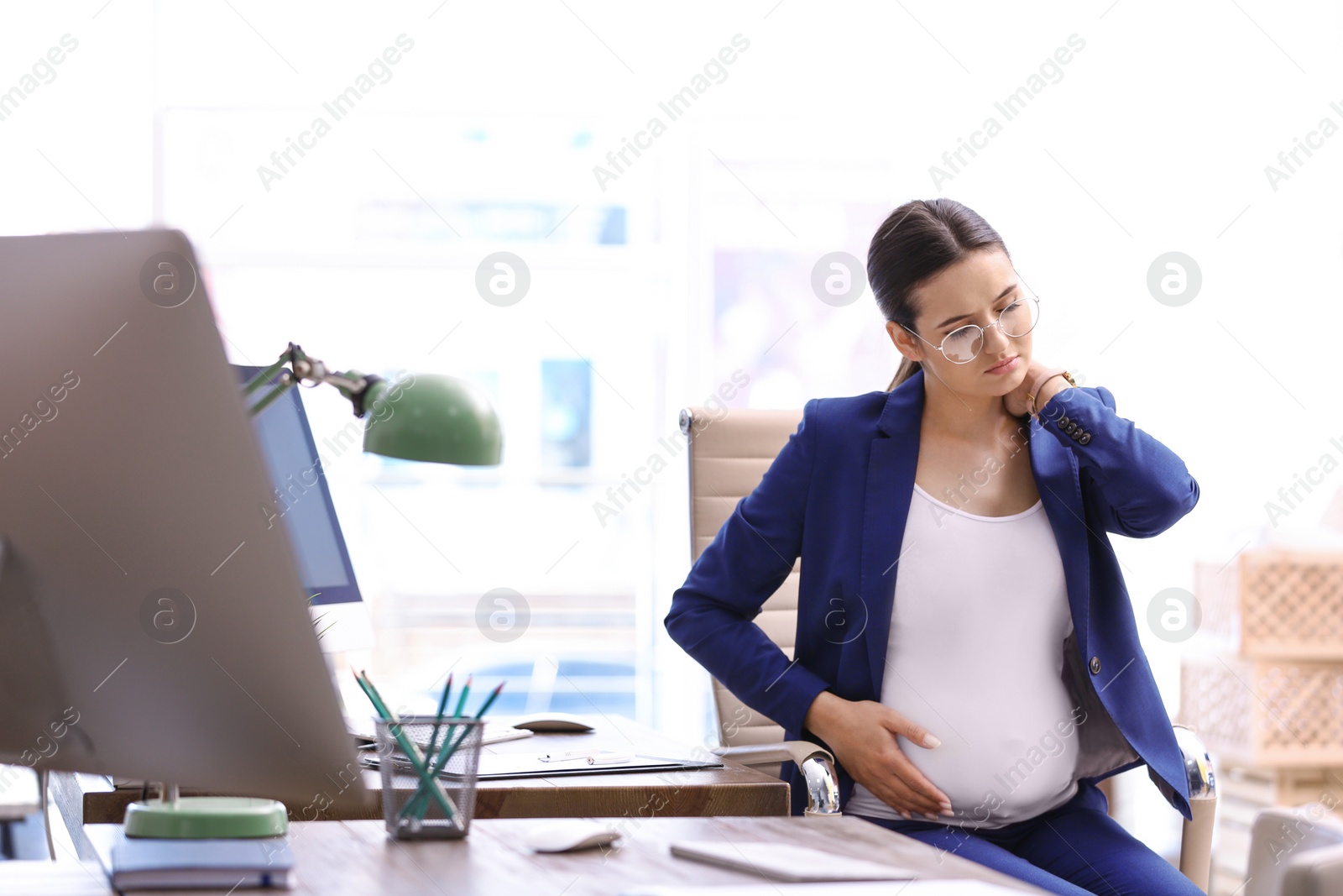 Photo of Young pregnant woman suffering from pain while working in office