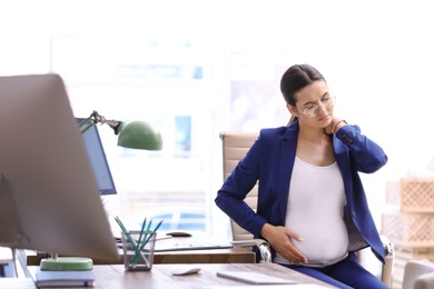 Photo of Young pregnant woman suffering from pain while working in office