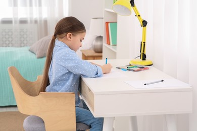 Photo of Cute little girl drawing with marker at desk in room. Home workplace