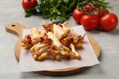 Photo of Delicious French fries with bacon, cheese sauce, tomatoes and herbs on light grey table, closeup