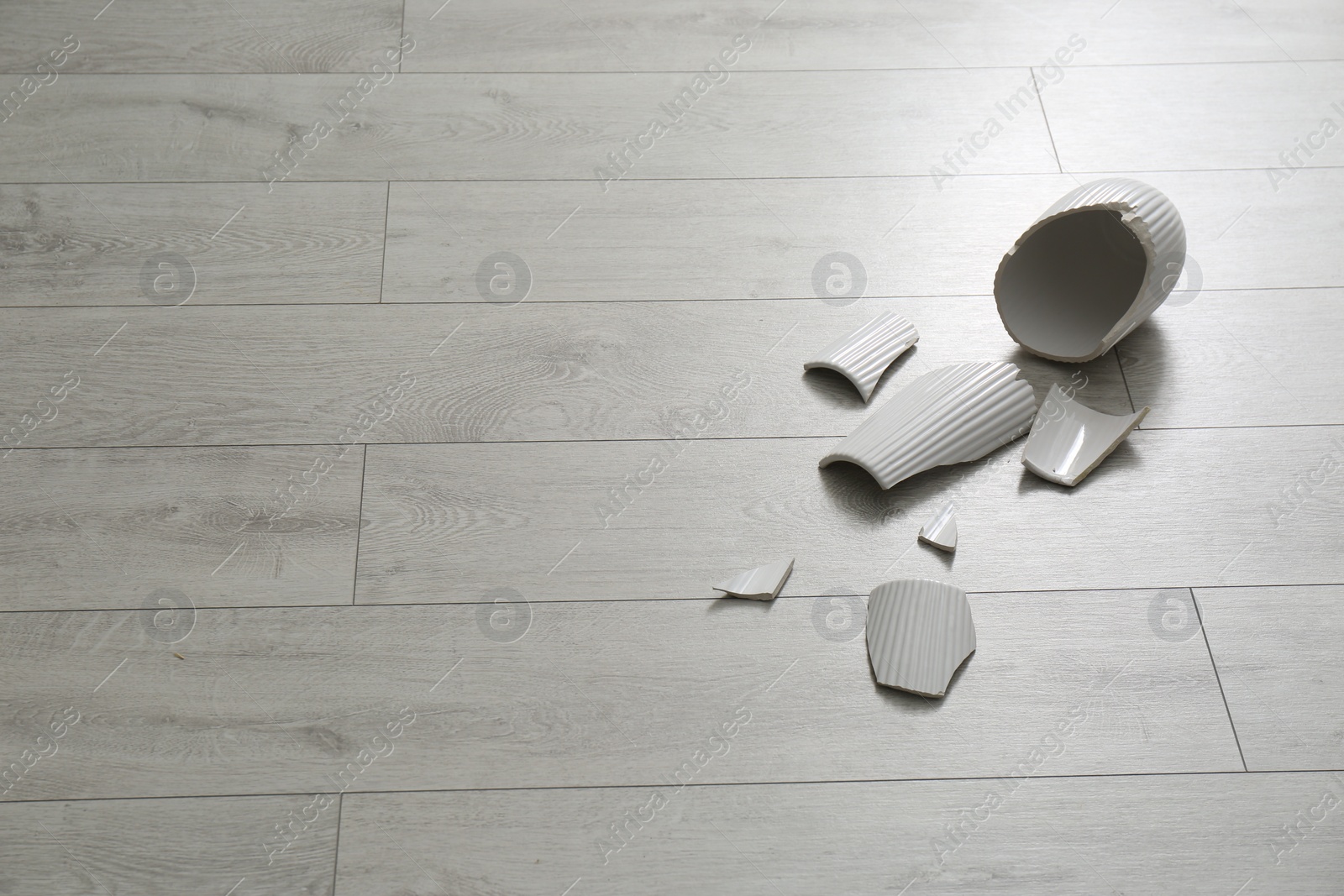 Photo of Broken ceramic vase on wooden floor. Space for text