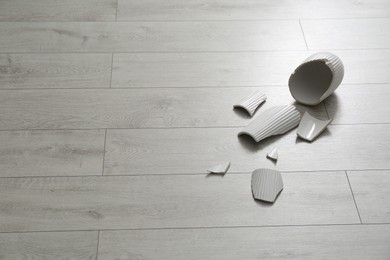 Broken ceramic vase on wooden floor. Space for text