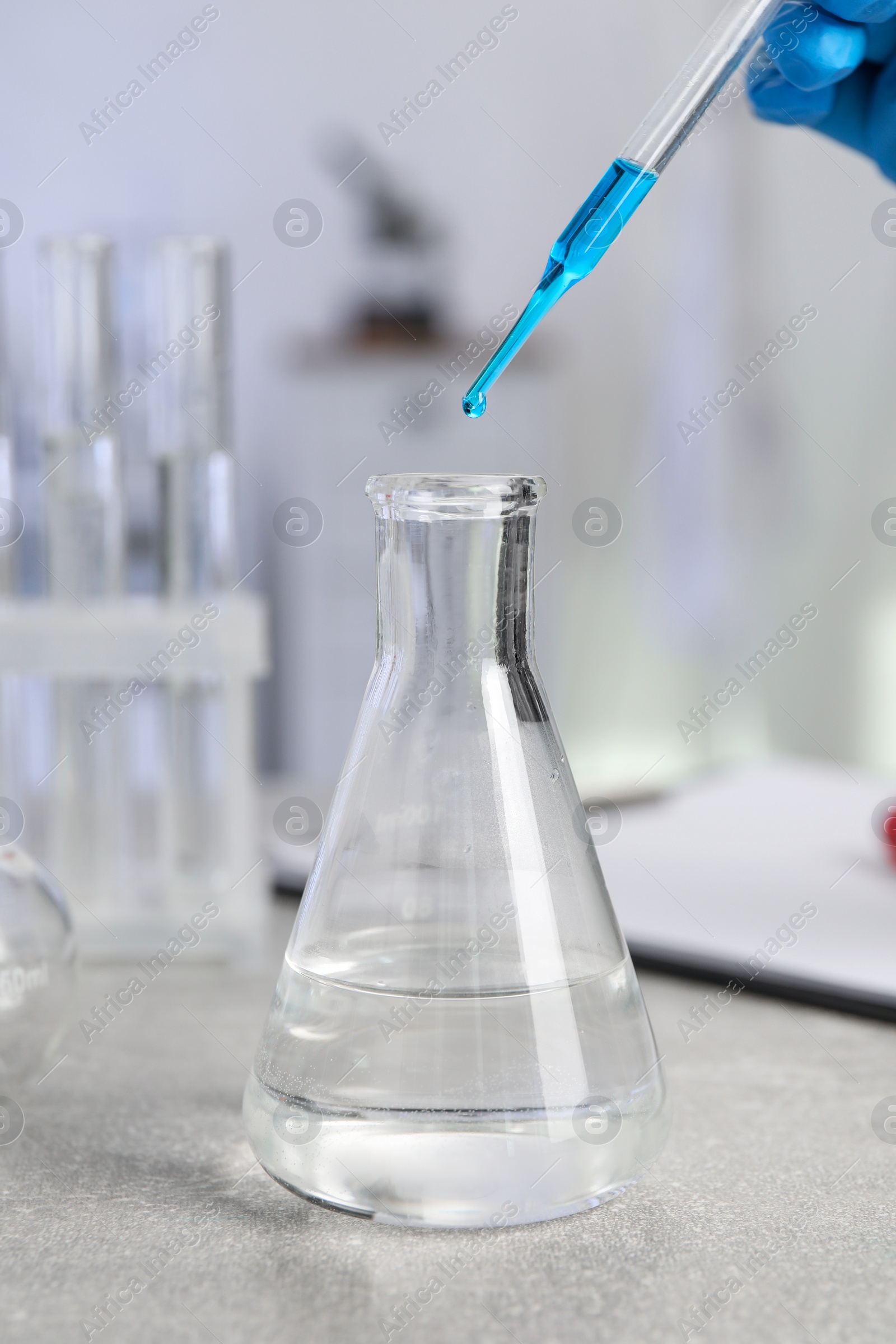 Photo of Laboratory analysis. Woman dripping liquid into flask at light grey table, closeup