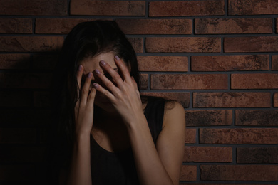 Photo of Crying young woman near brick wall. Domestic violence concept